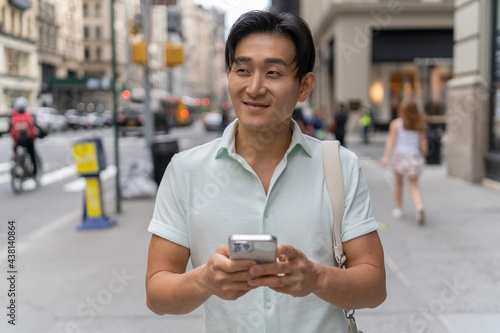 Young Asian man in city walking using cellphone