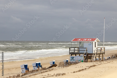 Beautiful beach on the German island of Sylt with white sand  cloudy dark sky  a lifeguard station and  beach chairs.