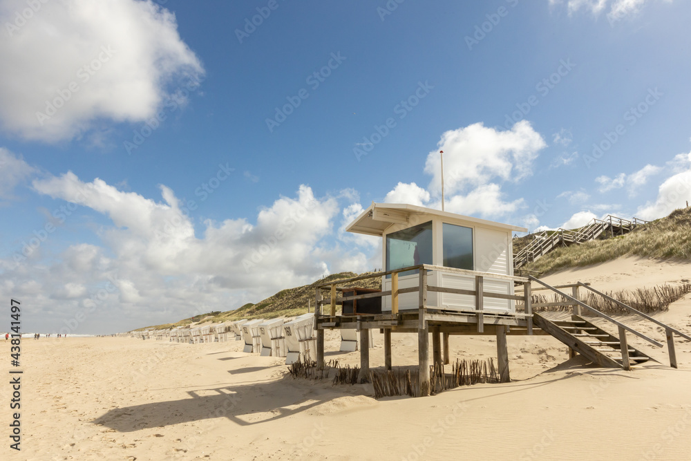empty beach chairs standing on an empty beach just behind a dune and a wooden jetty with an lifeguard house. an overcast sky over the blue sea and the sandy beach in the foreground. empty beach chairs standing on an empty beach just behind a dune and a wooden jetty with an lifeguard house. an overcast sky over the blue sea and the sandy beach in the foreground.