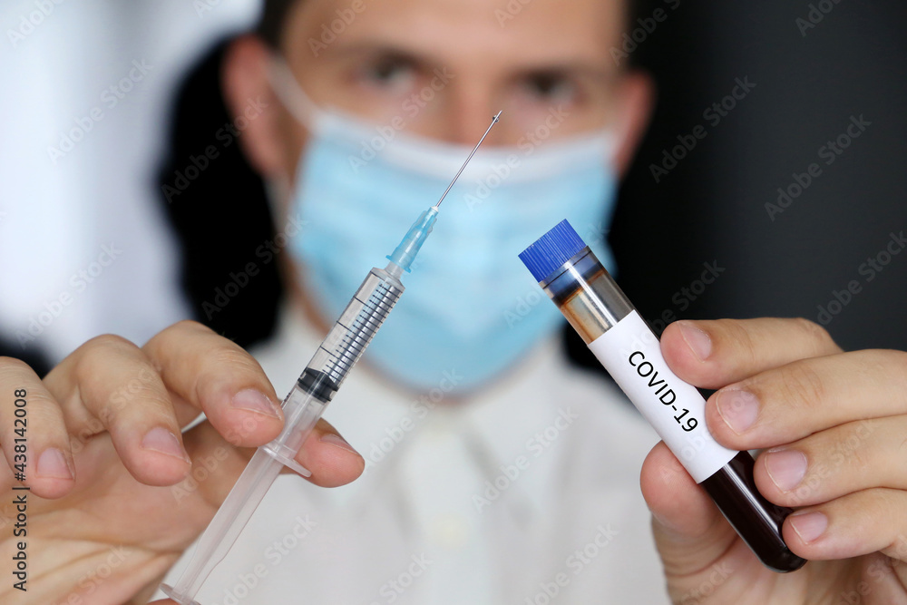 Doctor in mask with syringe and covid-19 blood sample in test tube in hands. Concept of vaccination and medical testing Doctor in mask with syringe and covid-19 blood sample in test tube in hands. Concept of vaccination and medical testing