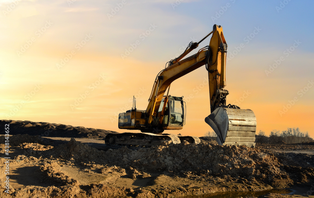 Excavator working on earthmoving at open pit mining on amazing sunset background. Backhoe digs sand and gravel in quarry. Heavy construction equipment during excavation at construction site Excavator working on earthmoving at open pit mining on amazing sunset background. Backhoe digs sand and gravel in quarry. Heavy construction equipment during excavation at construction site