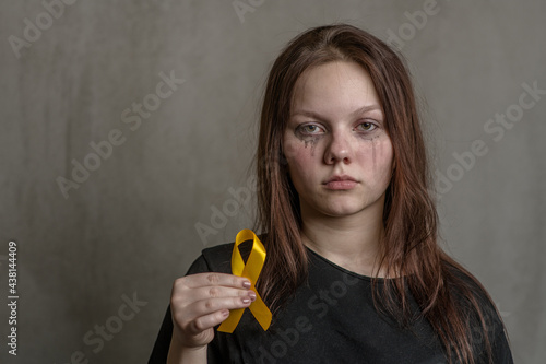 Tear-stained teen girl holds yellow ribbon. Concept of suicide problems and their prevention. Empty space for text