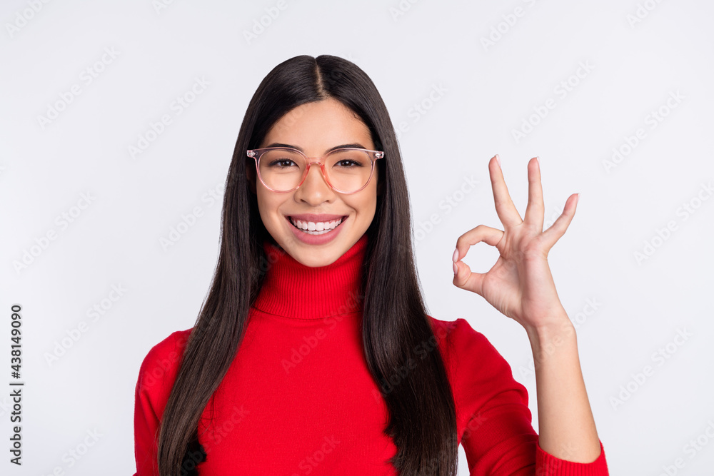 Photo of young smiling good mood charming asian girl in glasses show okay sign isolated on grey color background Photo of young smiling good mood charming asian girl in glasses show okay sign isolated on grey color background