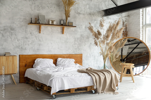 Spacious airy white eco style loft bedroom with bed,  mirror and pampas grass decoration