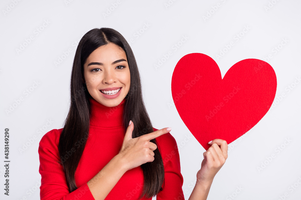 Photo of happy cheerful smiling positive girl point finger big red paper heart recommend isolated on grey color background Photo of happy cheerful smiling positive girl point finger big red paper heart recommend isolated on grey color background