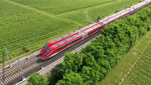 Two high-speed trains of red color moving towards the aerial view. The movement of trains between the vineyards top view.