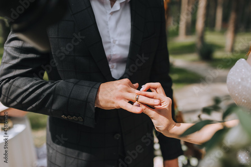 The groom at the wedding ceremony puts a gold ring on the bride's hand close-up.