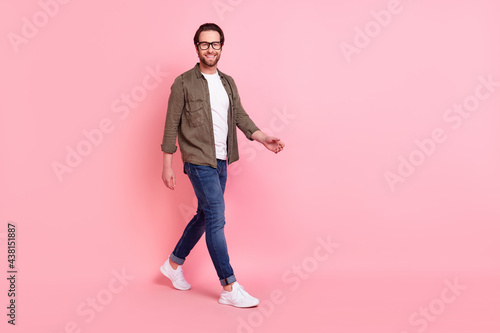 Photo of cute adorable young guy dressed brown shirt eyeglasses walking empty space smiling isolated pink color background