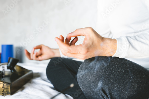 Man meditating in lotus position on bed. Focus on incense stick and smoke. Unrecognizable yoga practitioner in the background. Relax after Yoga training