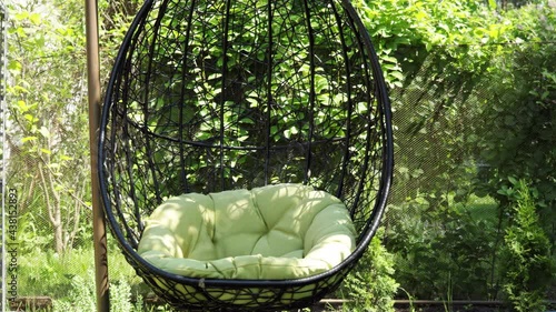 Coccoon chair sways in the wind  outside in the garden. Green nature and comfy sitting place. photo
