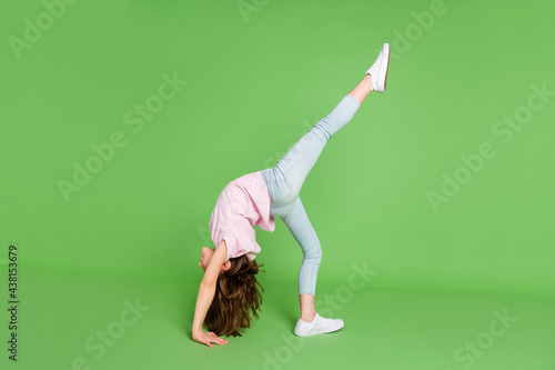 Full body profile side photo of young little girl stand bridge pose raise legs acrobat isolated over green color background photo