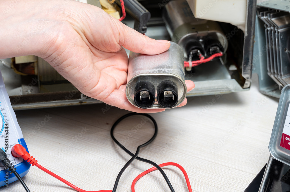 Repair of the microwave oven. A woman shows an old capacitor. Repair of the microwave oven. A woman shows an old capacitor.