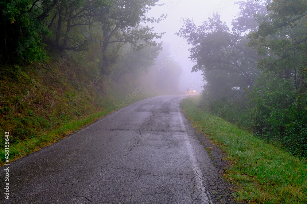 car in fog driving with lights on. Foggy road in the mountains across green forest, fog, cloudy sky car in fog driving with lights on. Foggy road in the mountains across green forest, fog, cloudy sky