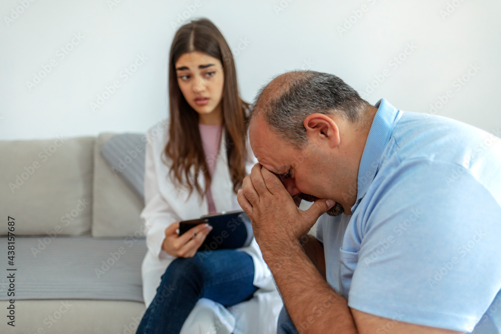 Distraught Caucasian man has head in his hands while talking with a healthcare professional. Unhappy man at the psychologist. Doctor or psychiatrist consulting and diagnostic examining stressful man. Distraught Caucasian man has head in his hands while talking with a healthcare professional. Unhappy man at the psychologist. Doctor or psychiatrist consulting and diagnostic examining stressful man.