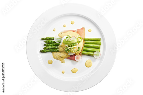 Delicious breakfast asparagus with poached egg, bacon, hollandaise sauce in a white plate. Isolated on white background. View from above