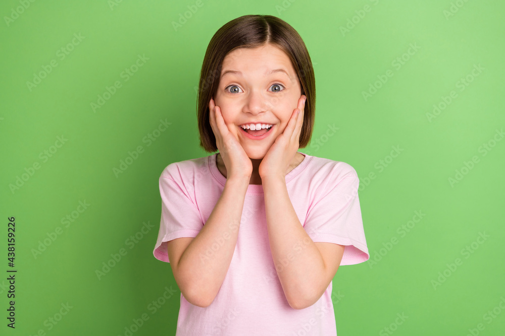 Photo of young little girl happy positive smile amazed shocked surprised hands touch cheeks isolated over green color background Photo of young little girl happy positive smile amazed shocked surprised hands touch cheeks isolated over green color background