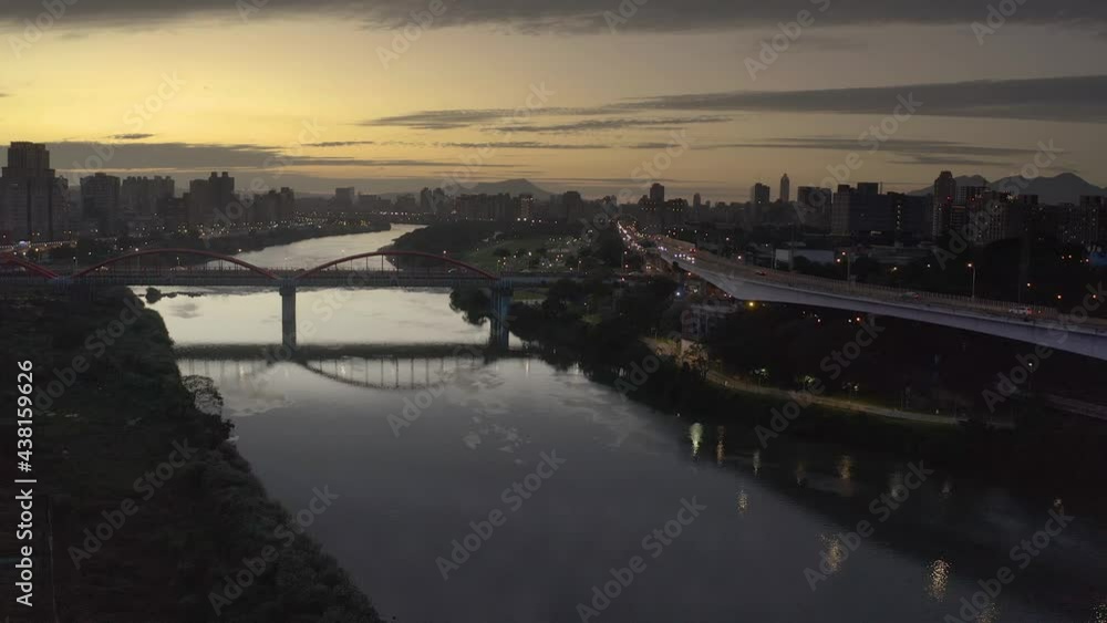 Slow aerial forward flight over reflecting river tamshui with bridge and crossing cars during sunset in Taipei. Skyline with skyscraper towers in background,Taiwan. Slow aerial forward flight over reflecting river tamshui with bridge and crossing cars during sunset in Taipei. Skyline with skyscraper towers in background,Taiwan.