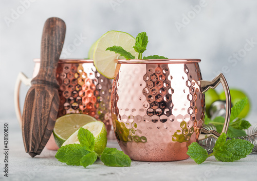 Photography Moscow mule cocktail in a copper mug with lime and mint and wooden squeezer on l