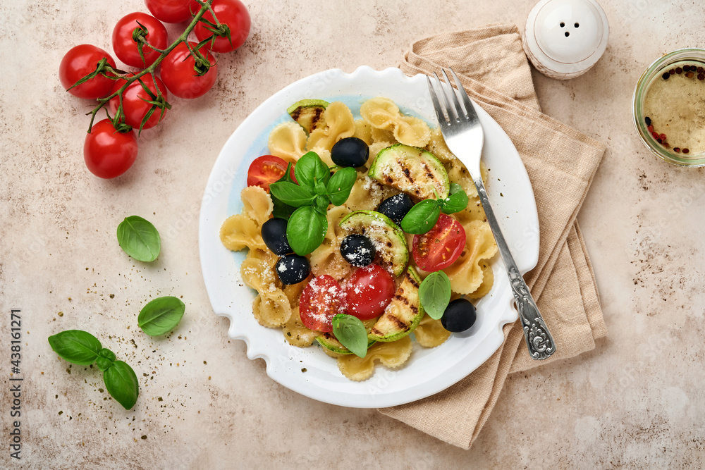 Pasta fiocchi salad with vegetables grilled zucchini, cherry tomato, olives, basil and parmesan cheese in white plate on light slate, stone or concrete background. Lunch concept. Top view Pasta fiocchi salad with vegetables grilled zucchini, cherry tomato, olives, basil and parmesan cheese in white plate on light slate, stone or concrete background. Lunch concept. Top view