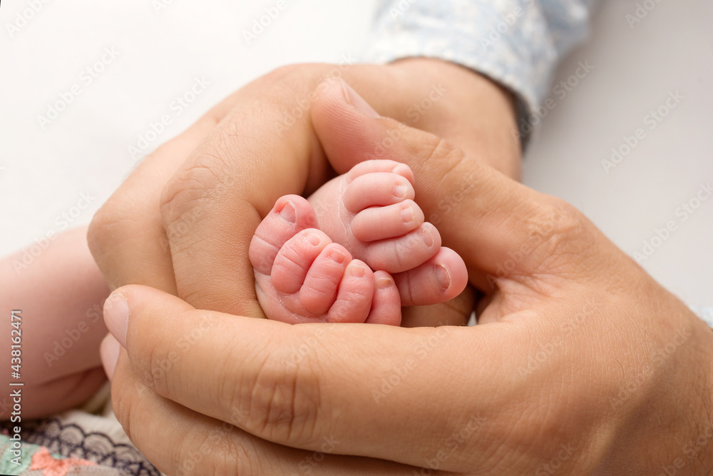 The father holds the bare feet of the newborn on a white background. Tiny legs in the hands of a man. Family, parents and homework concept. Health care, pediatrics. The father holds the bare feet of the newborn on a white background. Tiny legs in the hands of a man. Family, parents and homework concept. Health care, pediatrics.