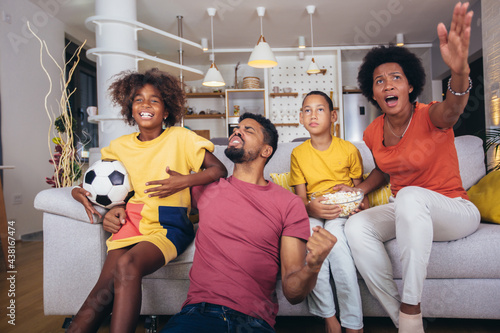 Happy african american family watching soccer match on television in living room at home.