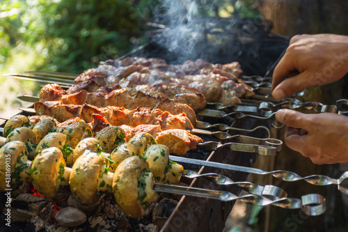 A man cooks marinated pork skewers and mushrooms on the grill in good sunny weather.