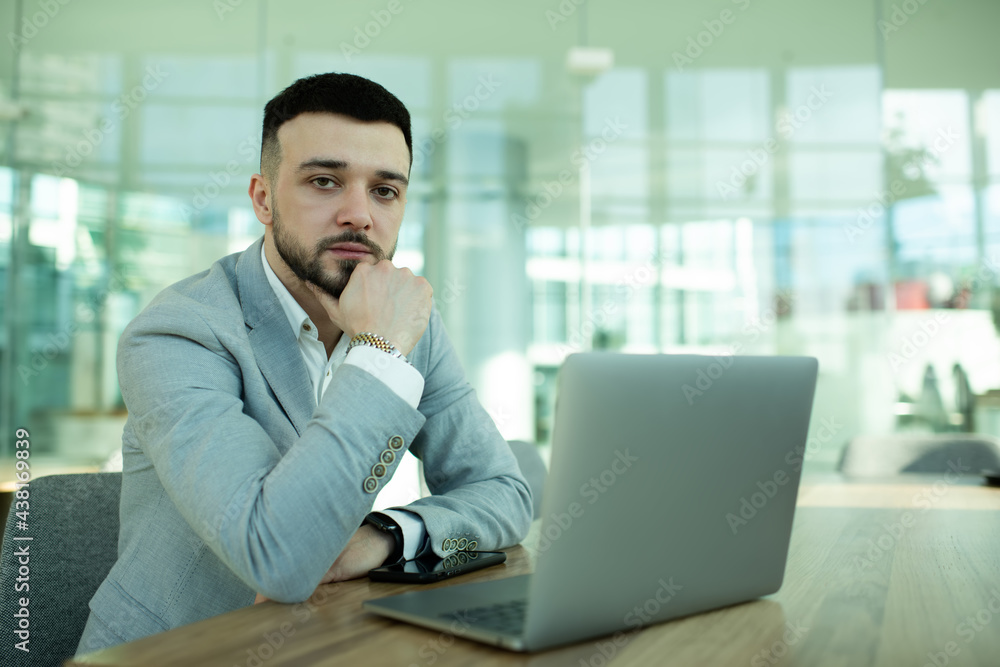 Pensive businessman working on laptop and touching chin in office Pensive businessman working on laptop and touching chin in office