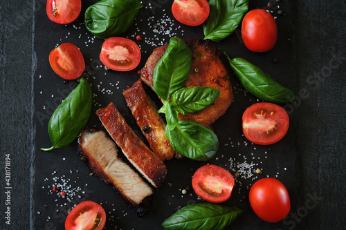 Appetizing steak with basil and tomatoes on a dark stone board.