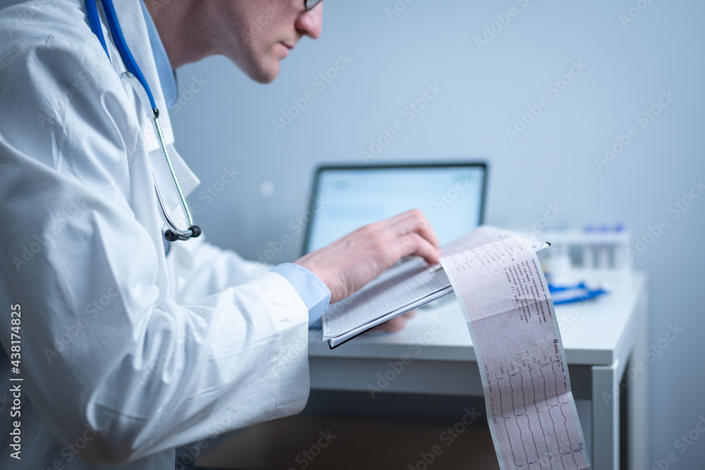 Cardiologist reading an ECG print-out. Doctor analyzing electrocardiogram. Practitioner examine patient test results. Medical and healthcare concept. Physician looking at cardiogram at medical office Cardiologist reading an ECG print-out. Doctor analyzing electrocardiogram. Practitioner examine patient test results. Medical and healthcare concept. Physician looking at cardiogram at medical office