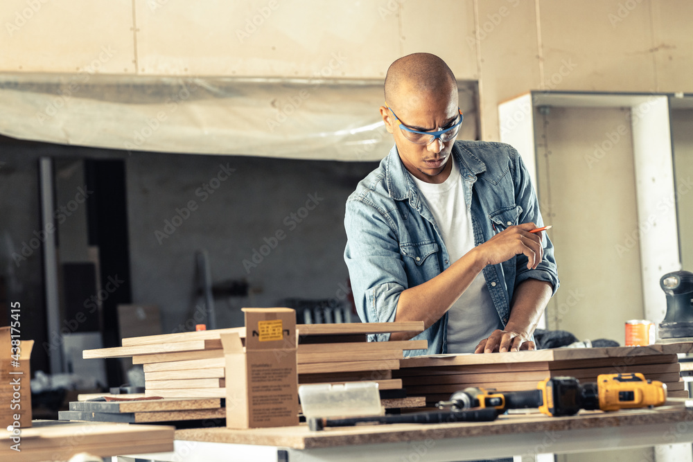 Young black man carpenter working in his workshop. He's examining the blueprint and preparing for work. Young black man carpenter working in his workshop. He's examining the blueprint and preparing for work.