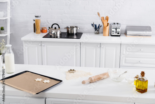 Dough, cookie cutter and rolling pin on table near flour in kitchen