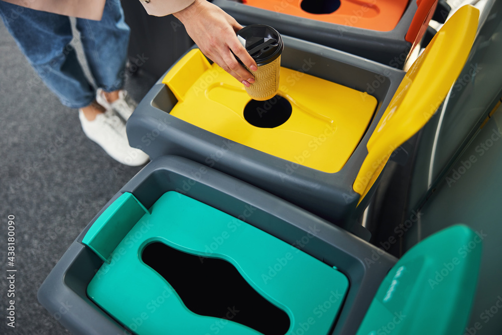 Female hand throwing coffee cup in trash can