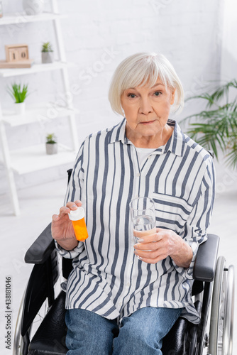 Senior woman with pills and water looking at camera in wheelchair