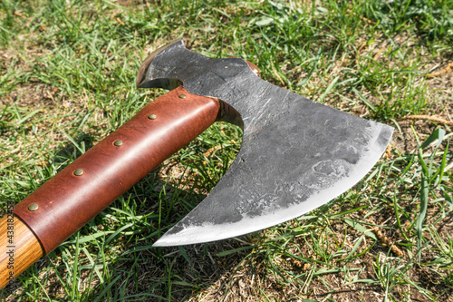 the battle ax is on the ground next to a large stone. forged ax