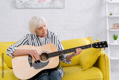 Senior woman playing acoustic guitar at home