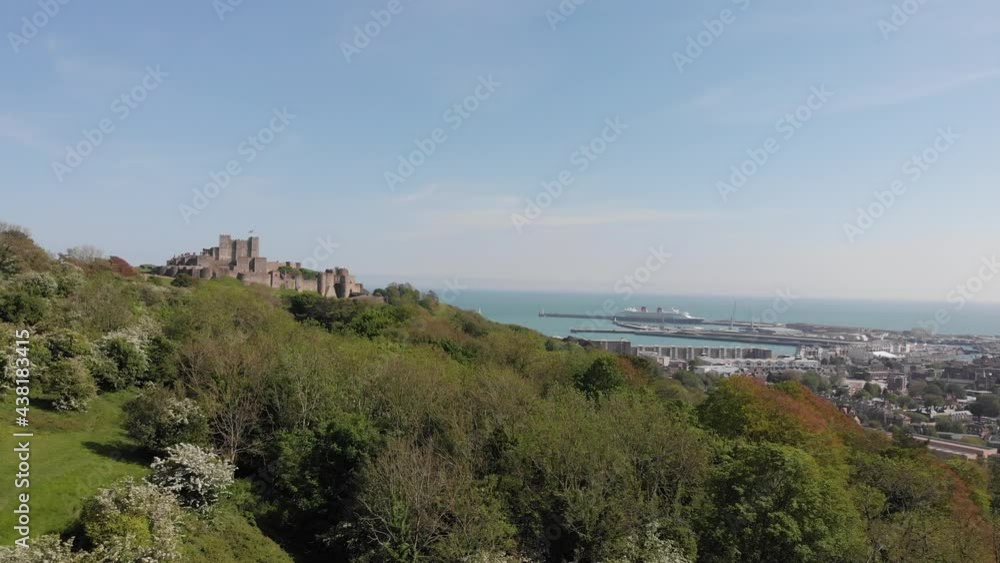 Forward motion drone shot towards Dover Castle in Kent UK with Dover ferry terminal and port with town and english channel with blue summer skies and white blooms on the trees. Forward motion drone shot towards Dover Castle in Kent UK with Dover ferry terminal and port with town and english channel with blue summer skies and white blooms on the trees.