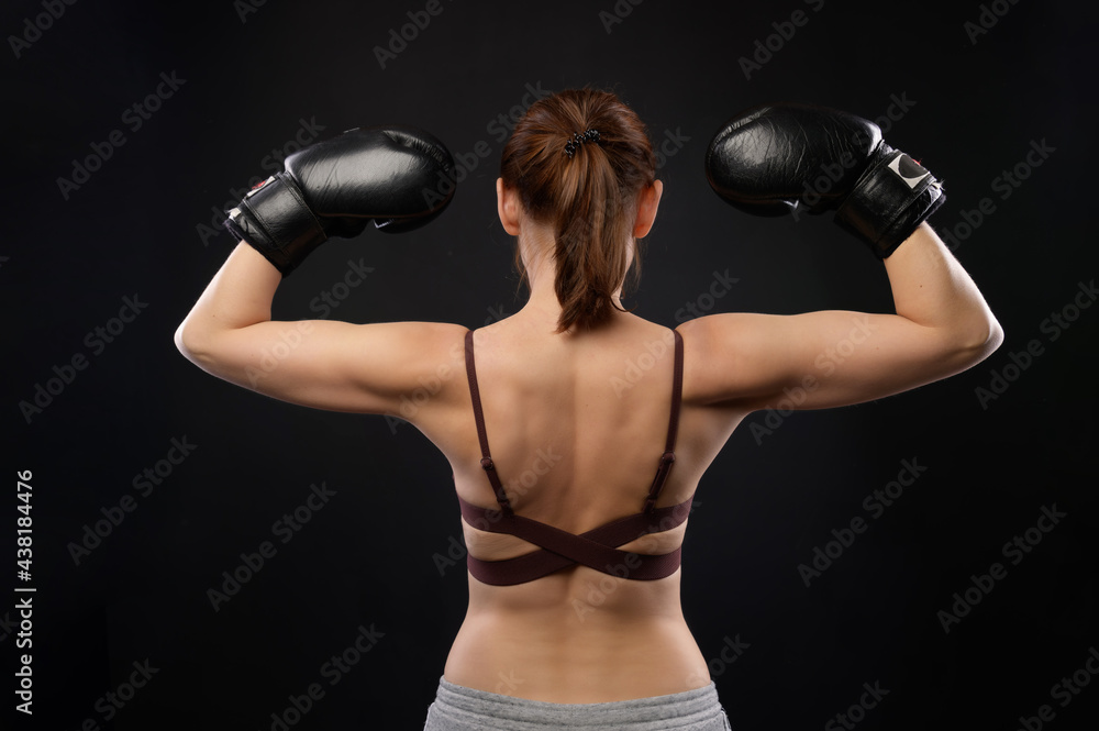 Portrait of a woman boxer with a backside. Caucasian woman in boxing gloves shows a gesture of strength. Studio photo Portrait of a woman boxer with a backside. Caucasian woman in boxing gloves shows a gesture of strength. Studio photo