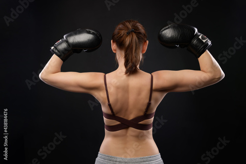 Portrait of a woman boxer with a backside. Caucasian woman in boxing gloves shows a gesture of strength. Studio photo © yanik88