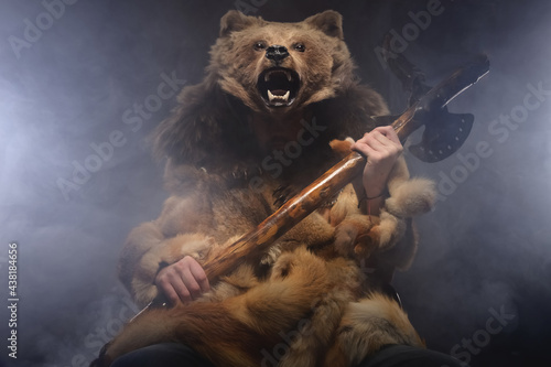 DreLh is a stylized male warrior with a beard in fur clothes with a bear s head and an ax in his hands sitting in the smoke. Studio photography