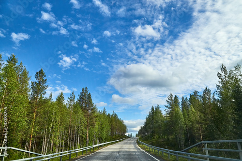 View from relief car windscreen on the blue sky with white clouds, grey asphalt road and landscape with forest and green teeses. Landscape through window