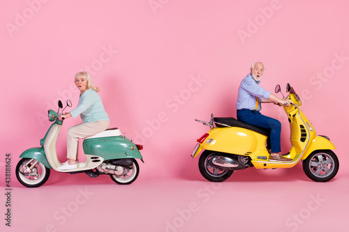 Full length profile side photo of two aged people amazed excited drive scooter speed isolated over pink color background