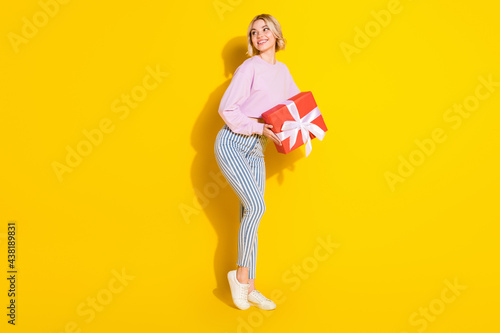 Full length photo of happy positive dreamy young woman look empty space hold present isolated on yellow color background © deagreez