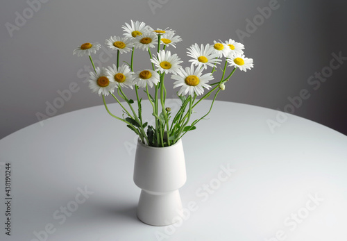 Fototapeta Naklejka Na Ścianę i Meble -  A bouquet of white daisies in a white vase on a white round table. Selective focus.