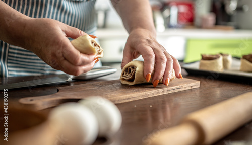 Woman in an apron in the kitchen is gently cutting fresh raw dough with a knife to make delicious homemade cinnamon rolls. Concept of the cooking process of baking