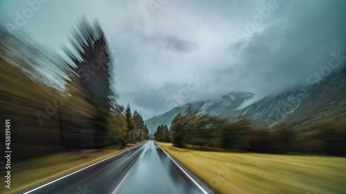 A speedy drive along the narrow asphalt road near the town of Sunndalsora, Norway. It is raining, the road is wet and black, blue-gray clouds hanging above. Mountains tower on the background. photo