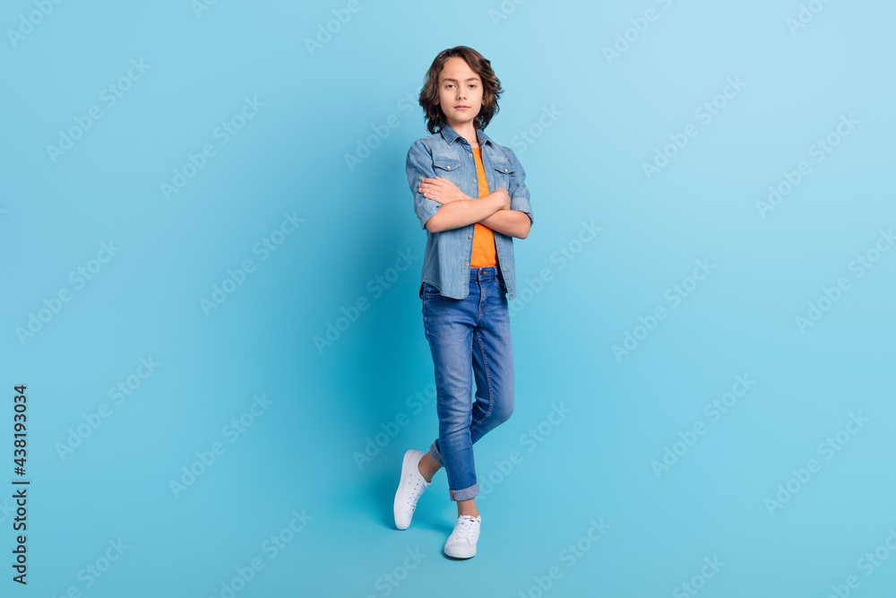 Full length photo of young school boy serious confident crossed hands isolated over blue color background Full length photo of young school boy serious confident crossed hands isolated over blue color background