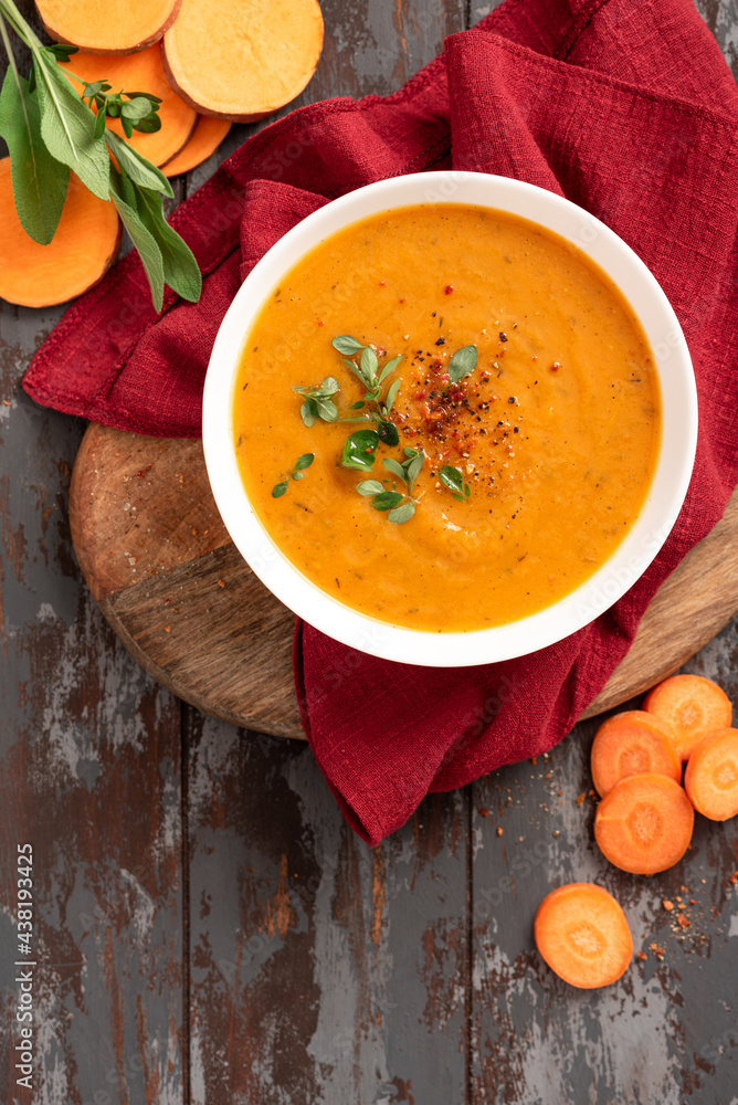 Creamy sweet potato soup with carrots and spices in a white bowl on a dark background top view. Tasty vegan sweet potato soup, autumn food. Creamy sweet potato soup with carrots and spices in a white bowl on a dark background top view. Tasty vegan sweet potato soup, autumn food.