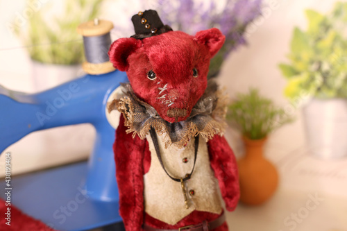Red teddy bear stand next to a sewing machine, fabric and thread, selective focus