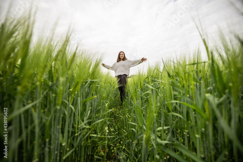 Happy woman staying with raised hands in green rye field and enjoys calm nature. Freedom and meditation concept. View from below