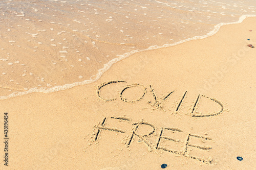 Covid free written on the shore, on the sand of a beach with wave washing the word, erasing or canceling it during Coronavirus summer, Covid free, safe beach, vaccine. Covid-19 immunity passport, pass